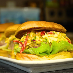Chef Winston's Floribbean Mango Burger Recipe with tropical mango-pineapple slaw, pepper jack cheese, Floribbean sauce, lettuce, tomato, and toasted brioche bun served for a Fourth of July summer cookout.
